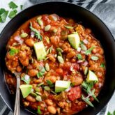 turkey chili in a black bowl from overhead with garnishes and avocado on top