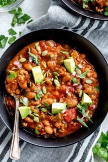 turkey chili in a black bowl from overhead with garnishes and avocado on top
