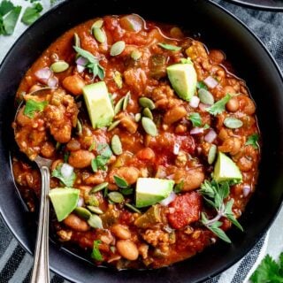 turkey chili with pinto beans in a black bowl with avocado on top