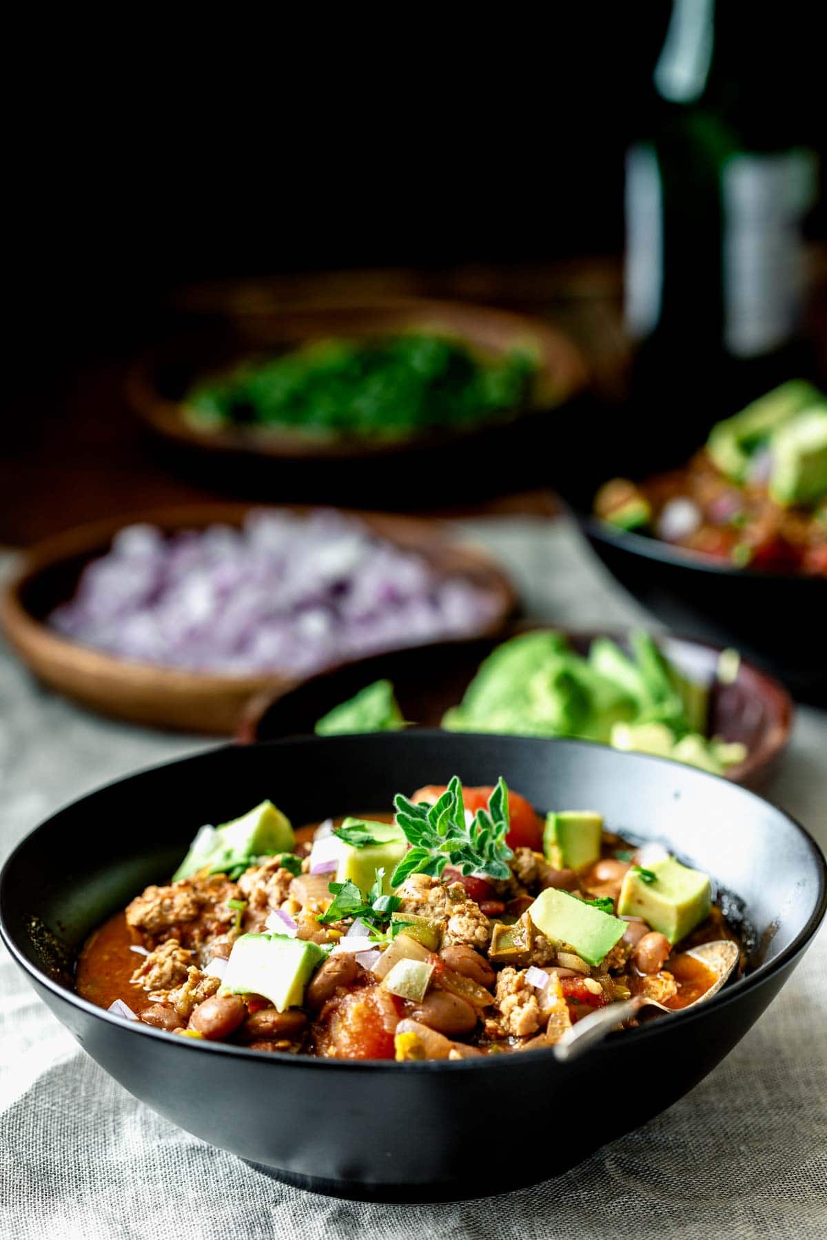 a bowl of chili on a table with bowls of toppings