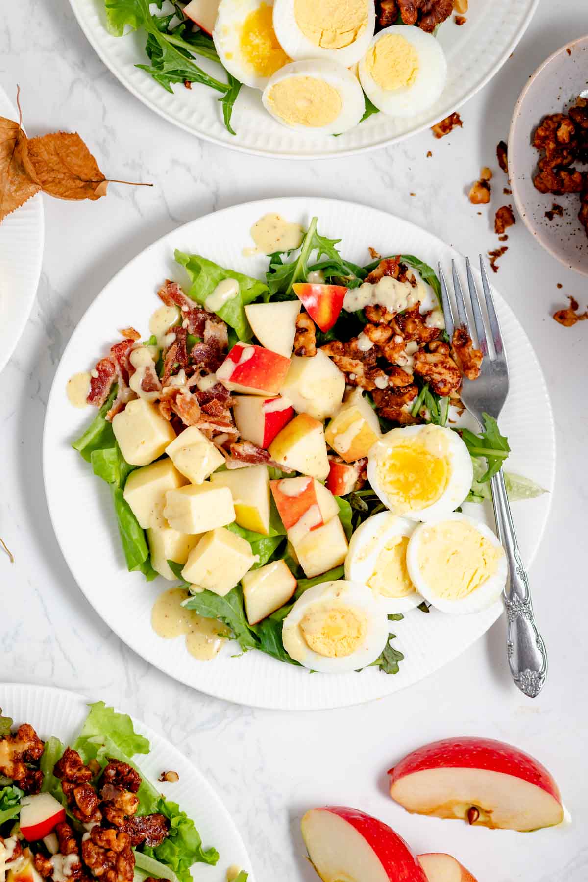 the composed harvest salad with a fork on a white plate on a white table with fall leaves