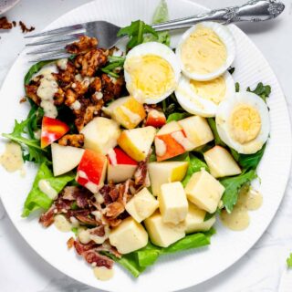 composed salad with eggs, chunks of cheddar and apple with a fork on a white plate