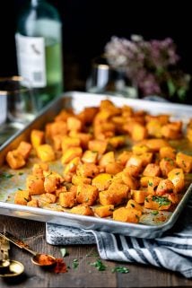 A sheet pan of roasted butternut squash with a bottle of white wine and a bouquet of sedum
