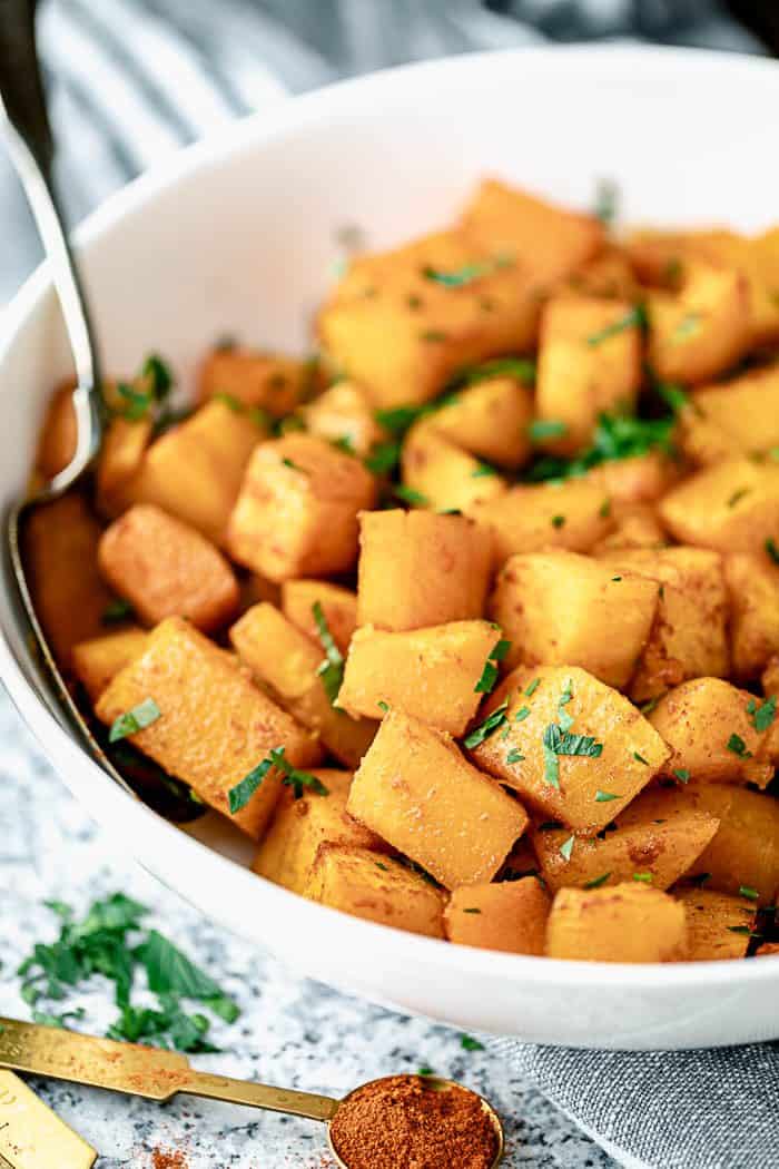 A side view closeup of a white serving dish with roasted butternut squash in it.