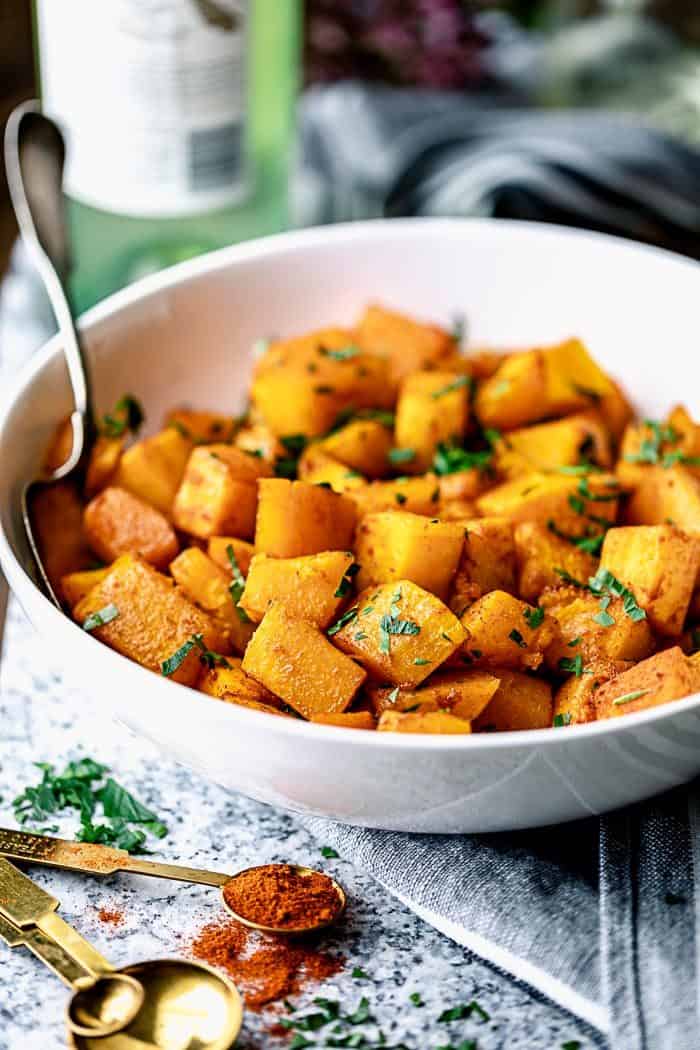 A side view closeup of a white serving dish with roasted butternut squash in it.