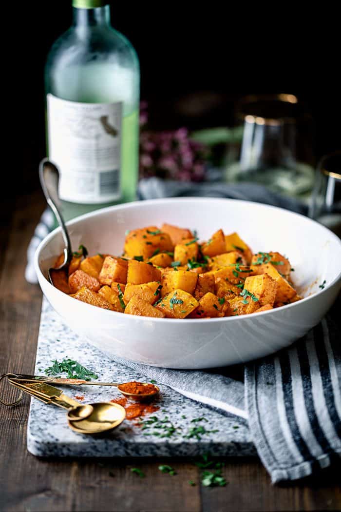 a side view of a serving bowl of butternut squash with smoked paprika with a dark background.