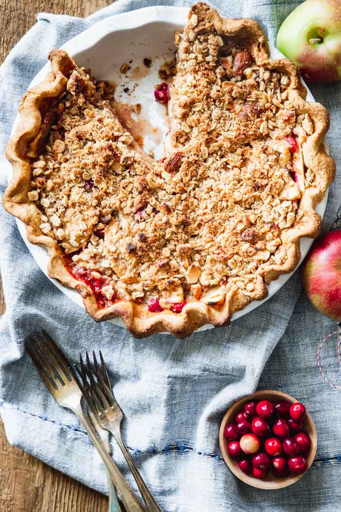 cranberry crumb apple pie overhead on a blue napkin with apples and cranberries beside it