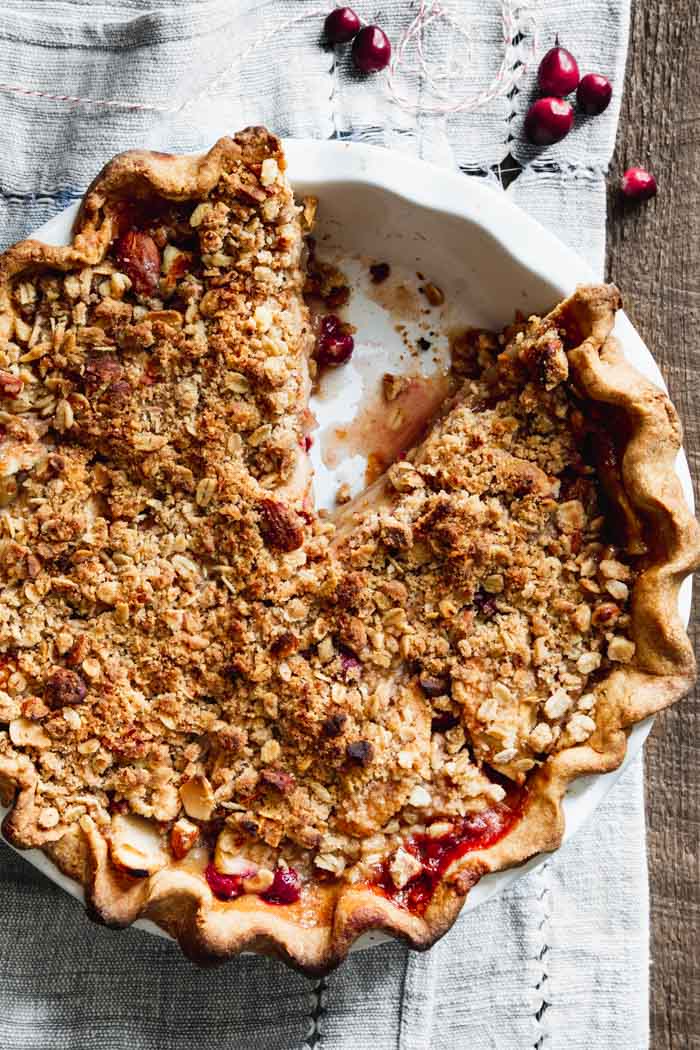 a crumble pie from overhead with a slice taken away, cranberries on the table surface