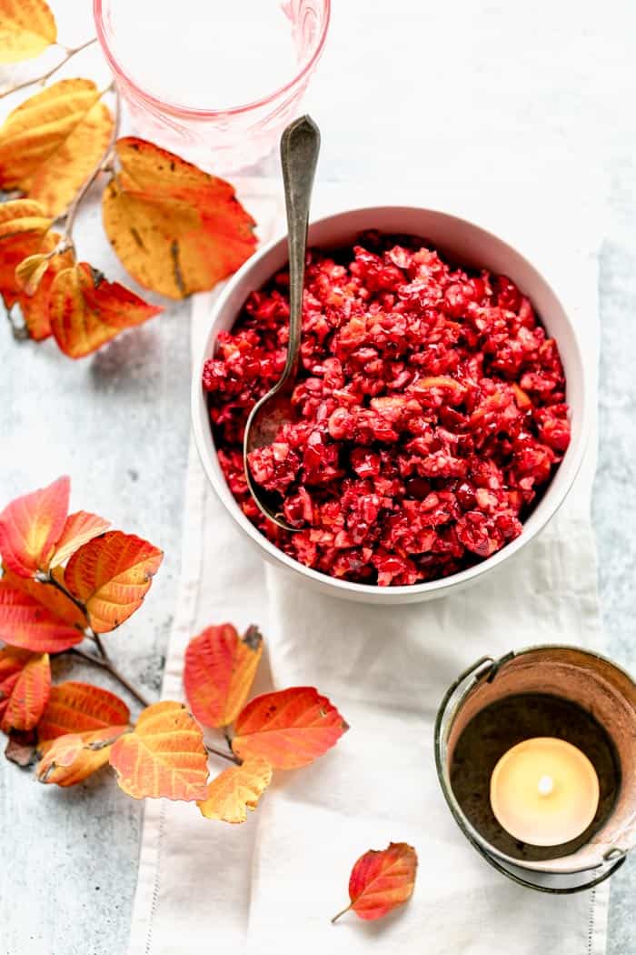 a table from overhead with a white linen, a votive candle and fall foliage with a bowl of cranberry relish