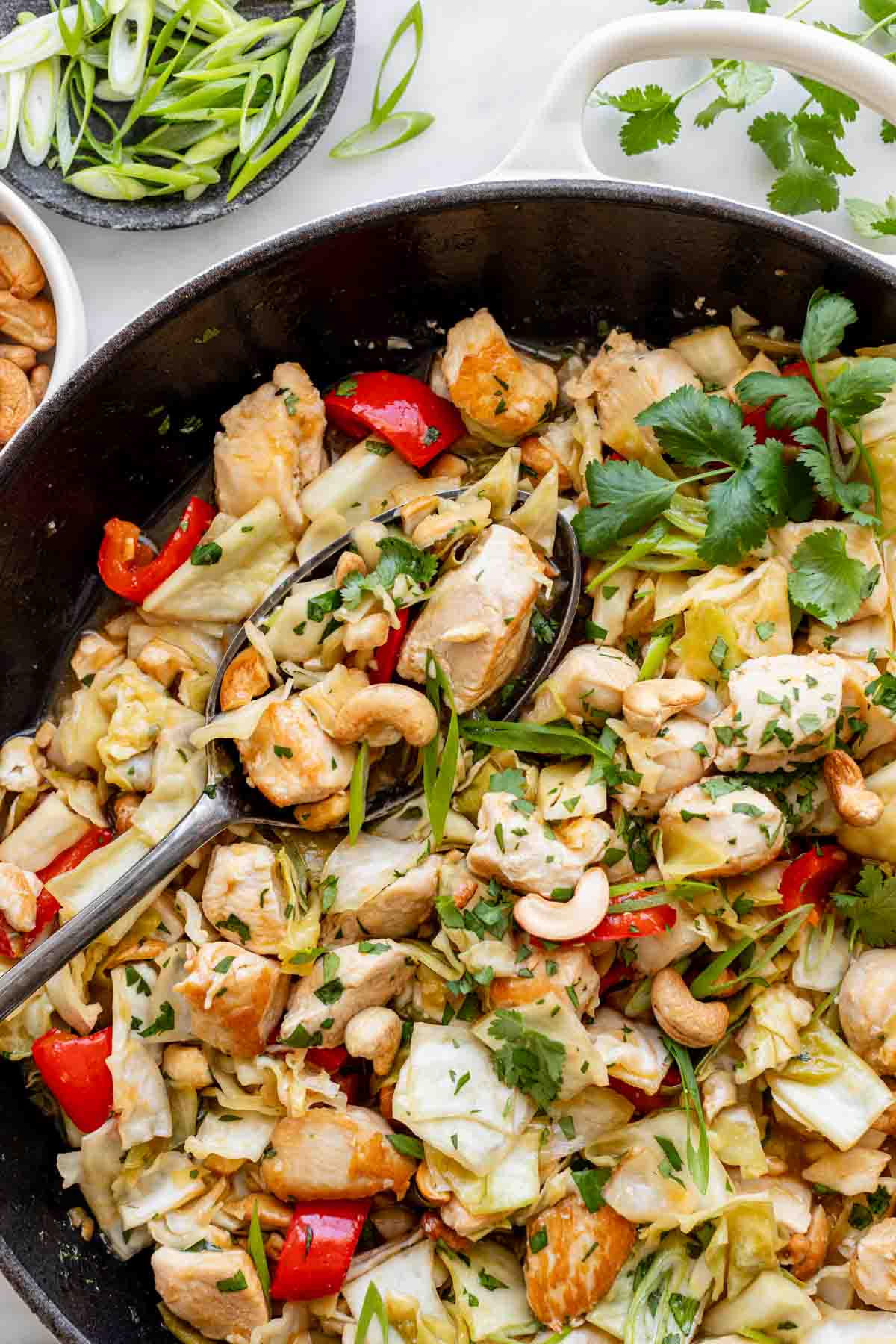 cabbage and chicken stirfried with bell pepper and cilantro in a black skillet with a white handle