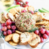 side view of cheeseball on a platter with crackers and grapes