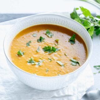 curry butternut squash soup in a white bowl with cilantro leaves on top