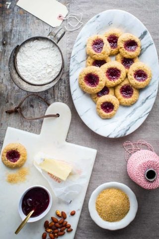 Jam Thumbprint Cookies on a platter surrounded by baking ingredients, red and white twine and gift tags