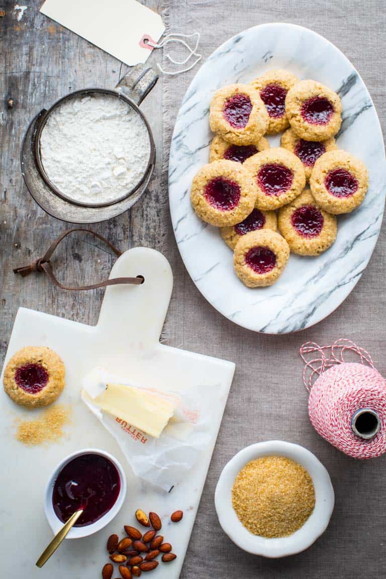 Jam Thumbprint Cookies on a platter surrounded by baking ingredients, red and white twine and gift tags
