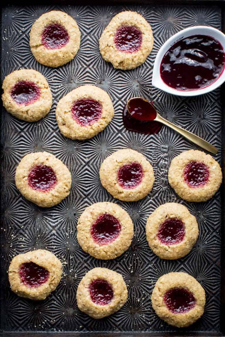 Jam Thumbprint Cookies and raspberry jam with a spoon on a dark baking sheet