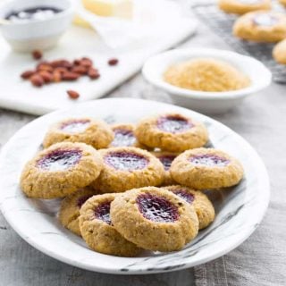 Jam Thumbprint Cookies on a platter surrounded by baking ingredients and cookies on a cooling rack