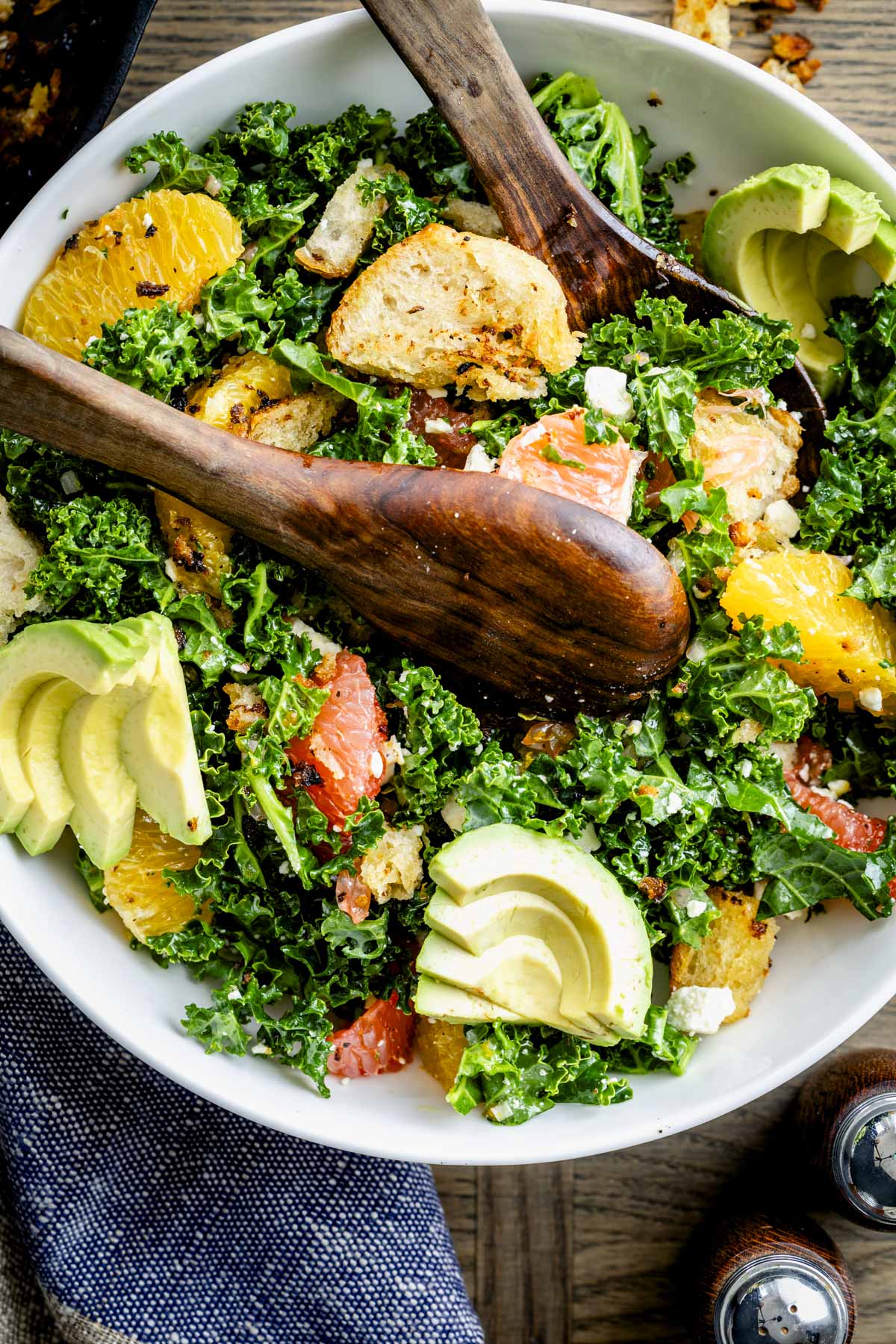 a white salad bowl with chopped kale salad with sliced avocado, oranges and grapefruit