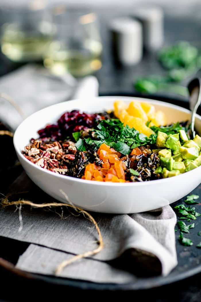 a side view of a Christmas table set with a bowl of wild rice salad with apricots, oranges, pecans and avocado.