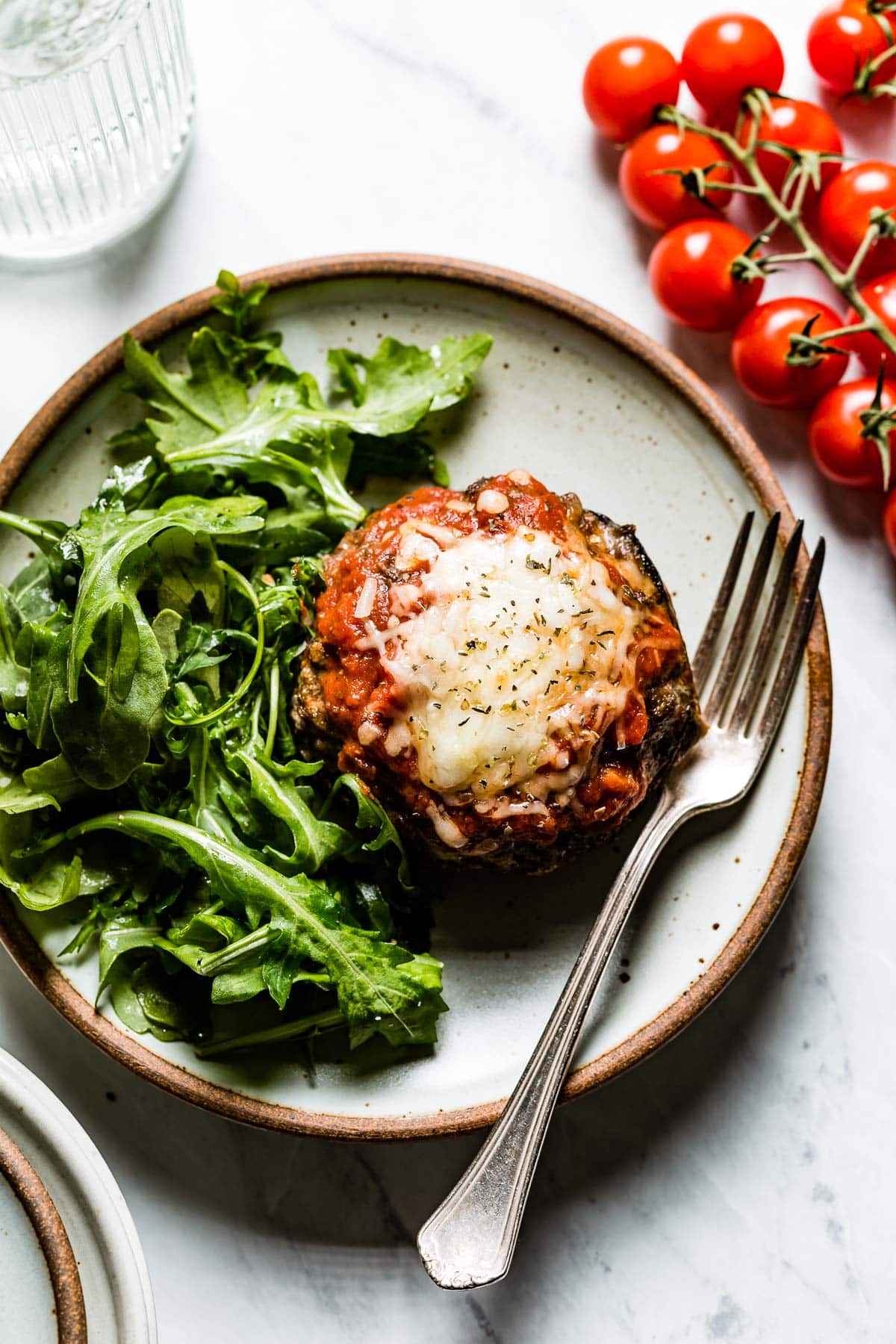 a plate with arugula salad and stuffed mushroom with tomato sauce and cheese melted on top