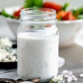 a jar of the dressing from the side with a bowl of salad in the background