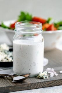 a jar of the dressing from the side with a bowl of salad in the background