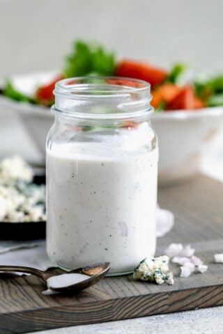 a jar of the dressing from the side with a bowl of salad in the background