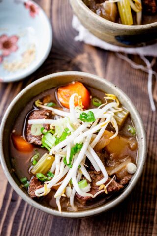 closeup into the bowl from overhead. The stew is topped with scallions, sprouts and sesame seeds.