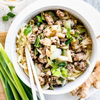 close-up of white bowl with pork stir-fry over noodles