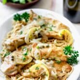 a white platter with chicken piccata, noodles and a bottle of wine