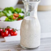 italian salad dressing in a jar on a table with salad in a bowl in the background.
