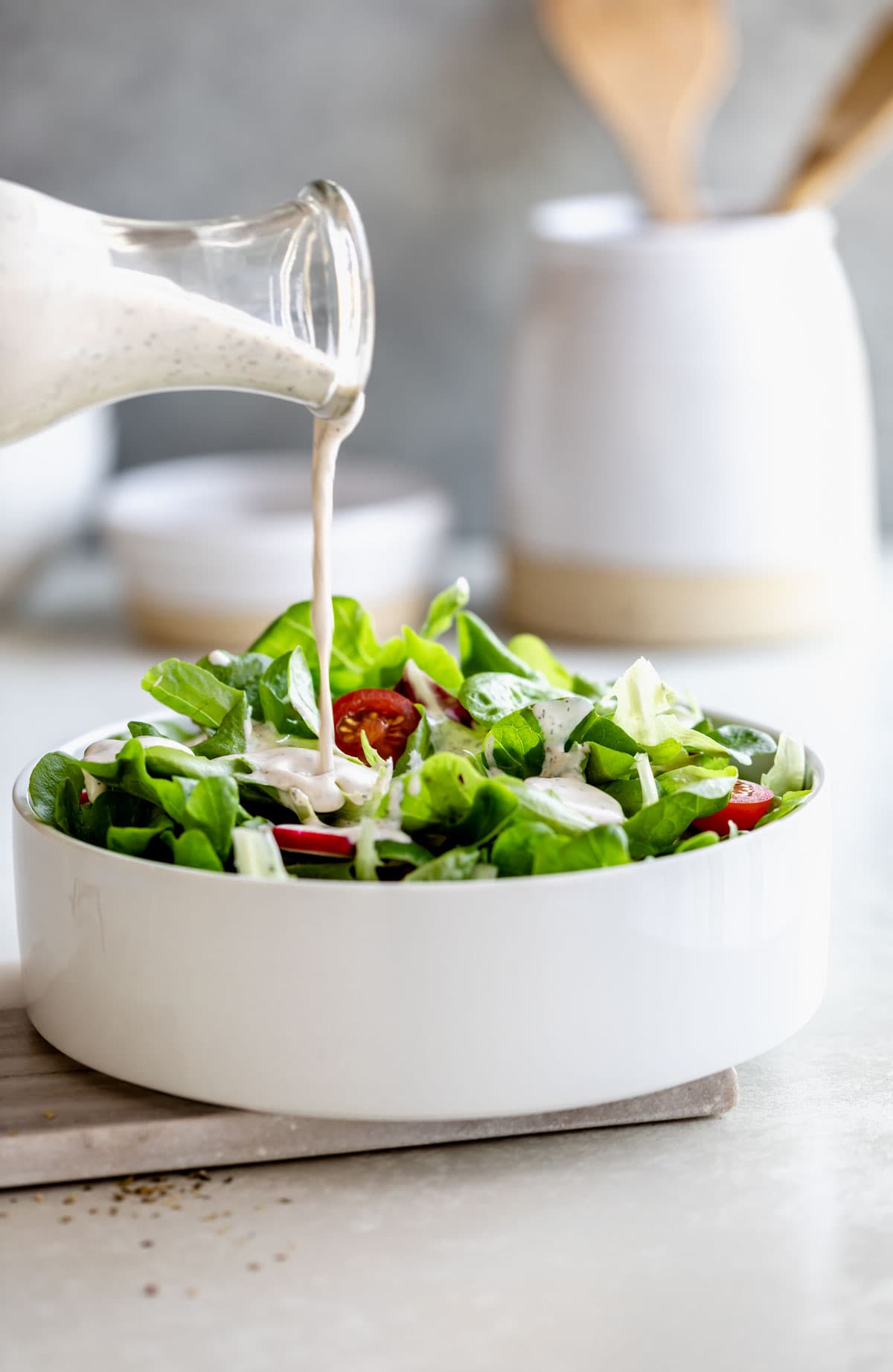 Italian dressing is being poured from a jar into a leafy salad in a white bowl.