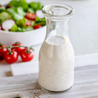 Italian salad dressing in a jar on a table with salad in a bowl in the background.