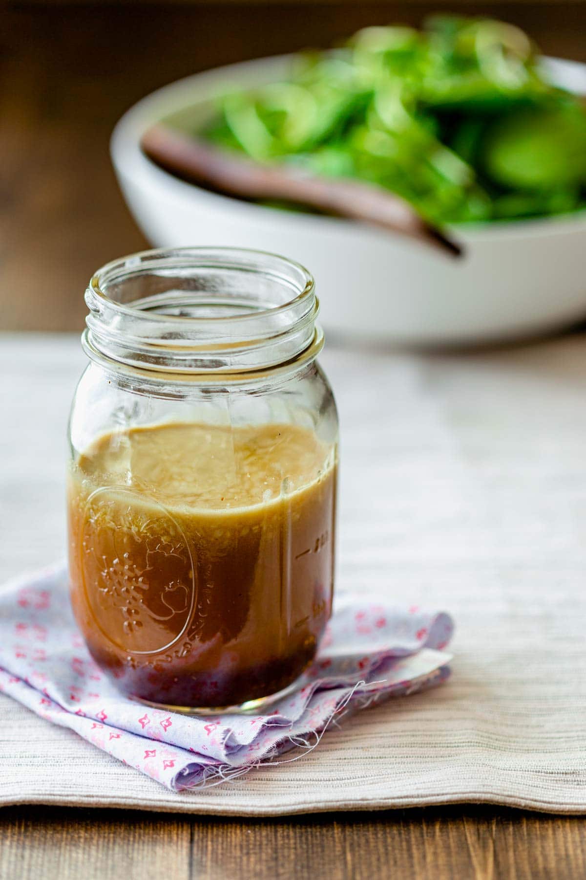 the dressing in a jar from the side with a salad behind it in a white bowl