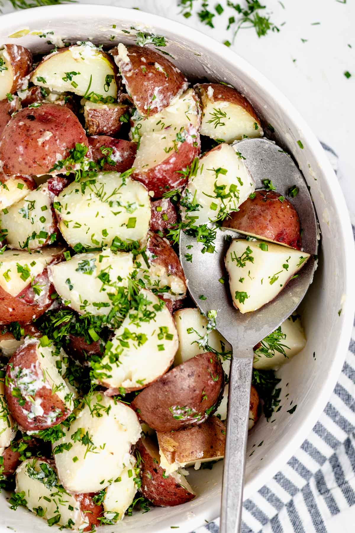 Close -up overhead shot of steamed potatoes with fresh herbs in a circular white bowl.