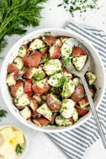 Steamed potatoes with fresh herbs in circular white bowl.