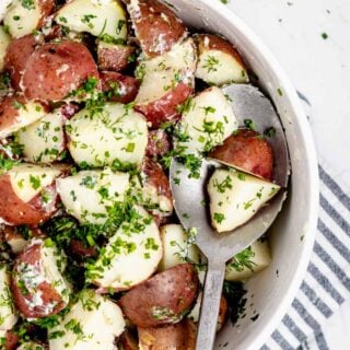 Close-up overhead shot of steamed potatoes with fresh herbs in a circular white bowl.