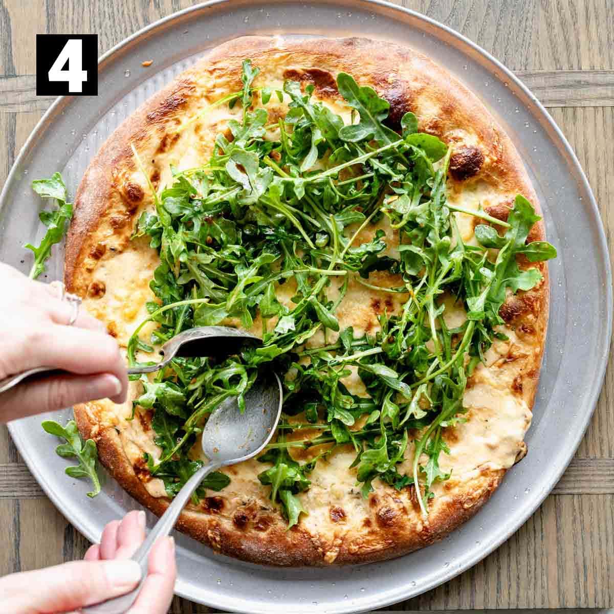 adding the raw arugula salad to the top of the baked pizza