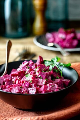 Chopped beets in a black bowl on a wooden table from the side