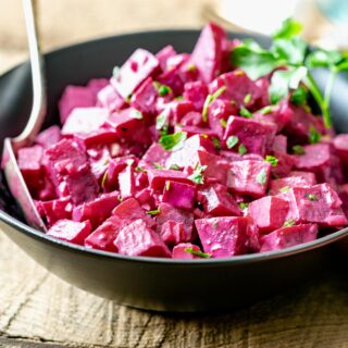 close up of beets with creamy tahini dressing from the side in a black bowl