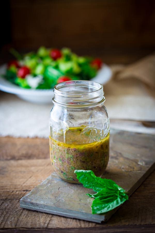 Olive salad dressing in mason jar with salad in a bowl in the background