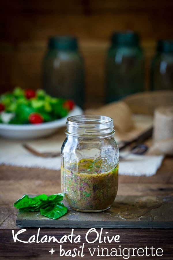 Olive salad dressing in mason jar with salad in a bowl in the background