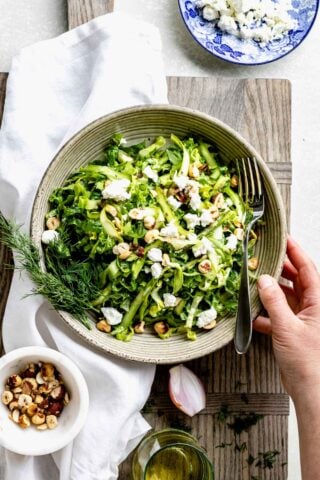 a bowl of shaved raw asparagus salad with a hand holding the bowl