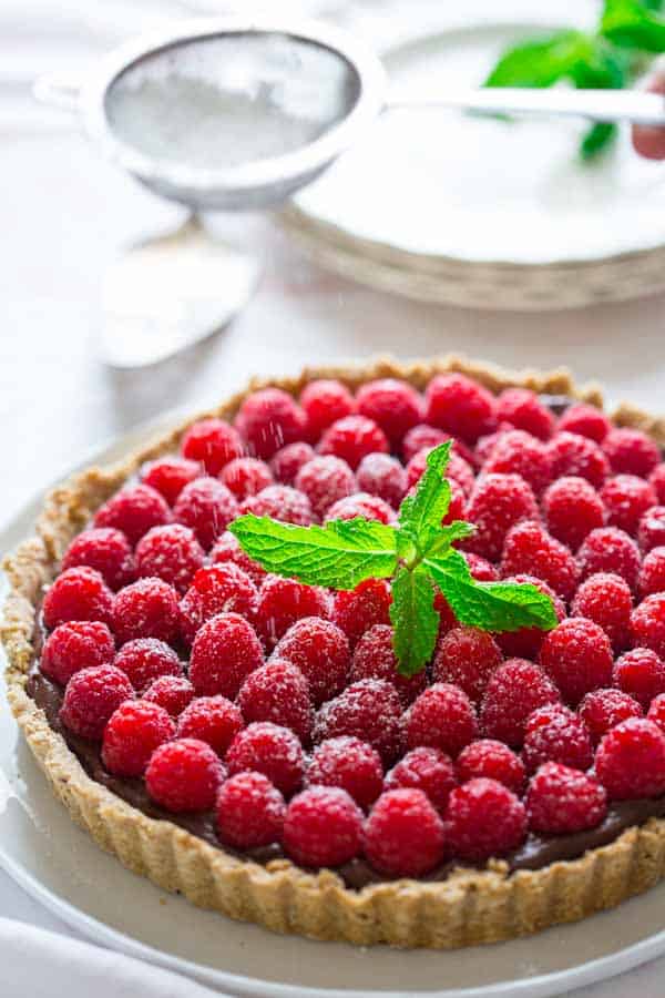 dusting powdered sugar over Chocolate Hazelnut Raspberry Tart