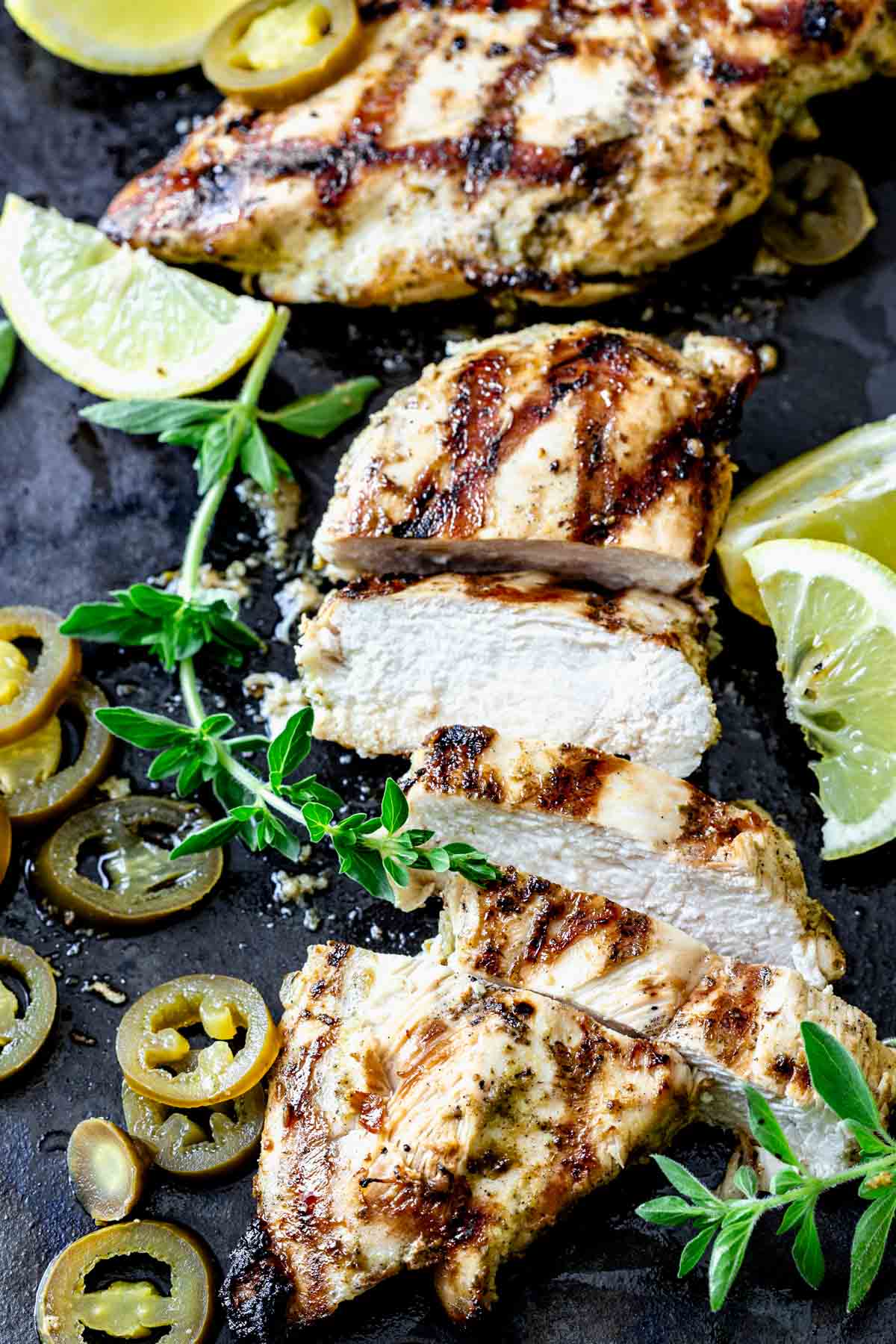 grilled chicken on a black surface, sliced with sprigs of oregano