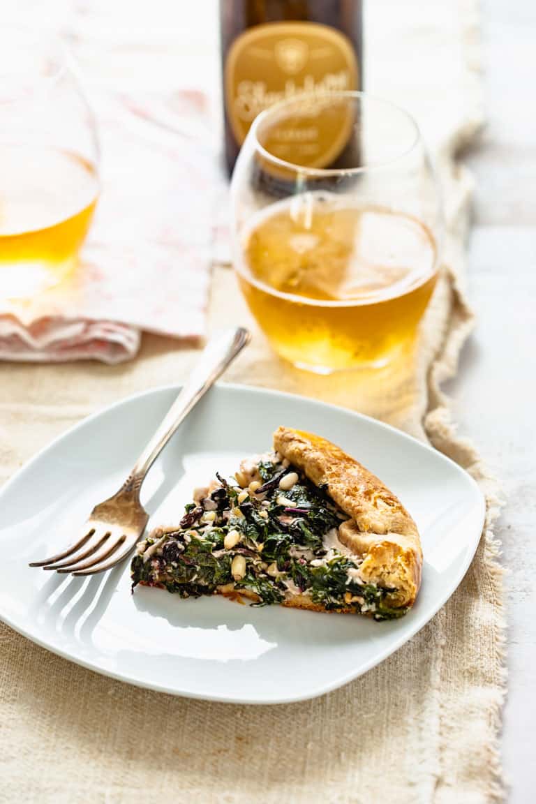 a slice of galette on a plate with a glass of hard cider