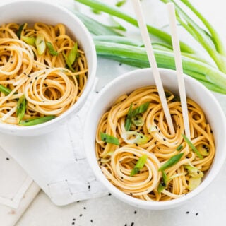 a close up of sesame noodles in two bowls with chopsticks