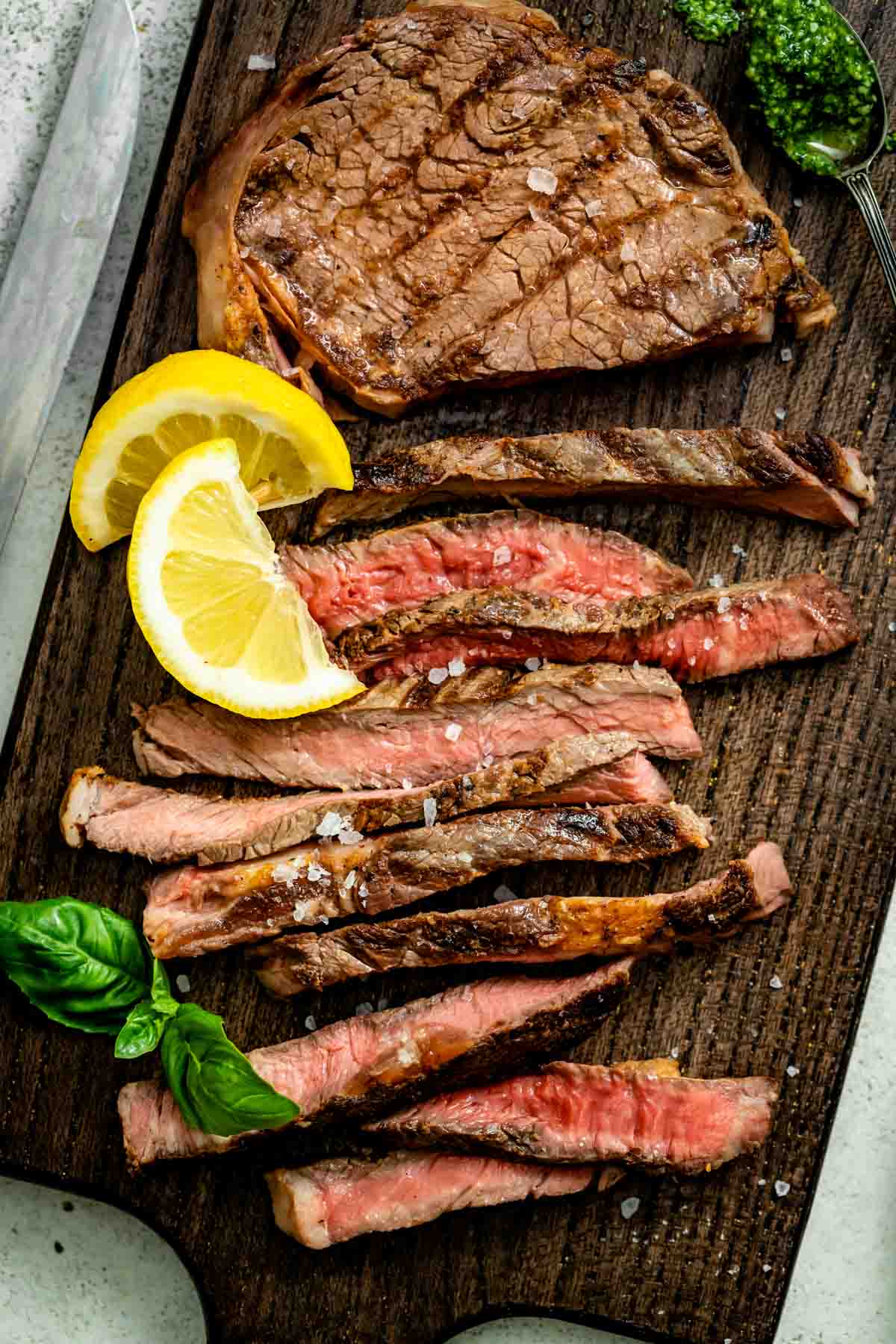 the grilled steak, sliced on a carving board with lemon