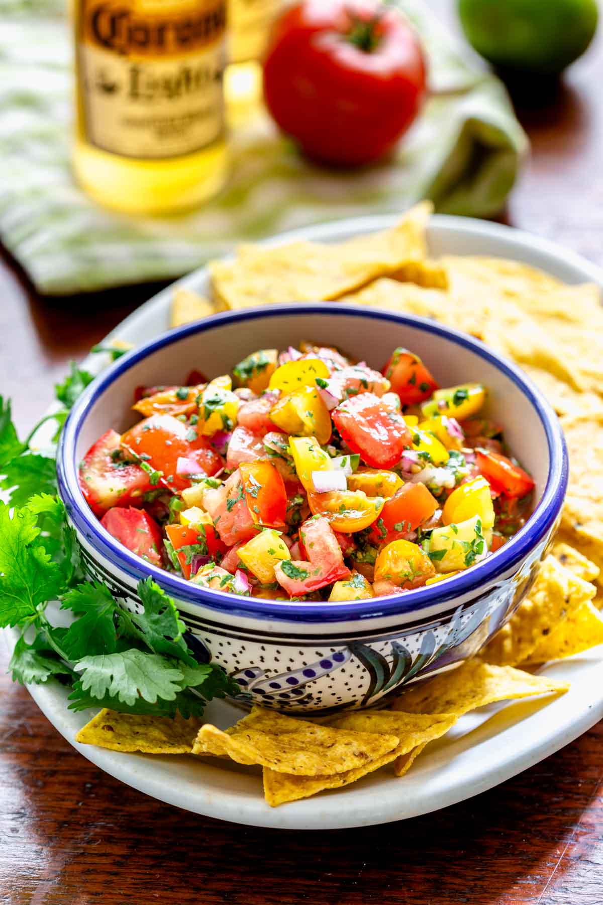 pico de gallo with red and yellow tomatoes in a blue and white bowl with chips and a beer