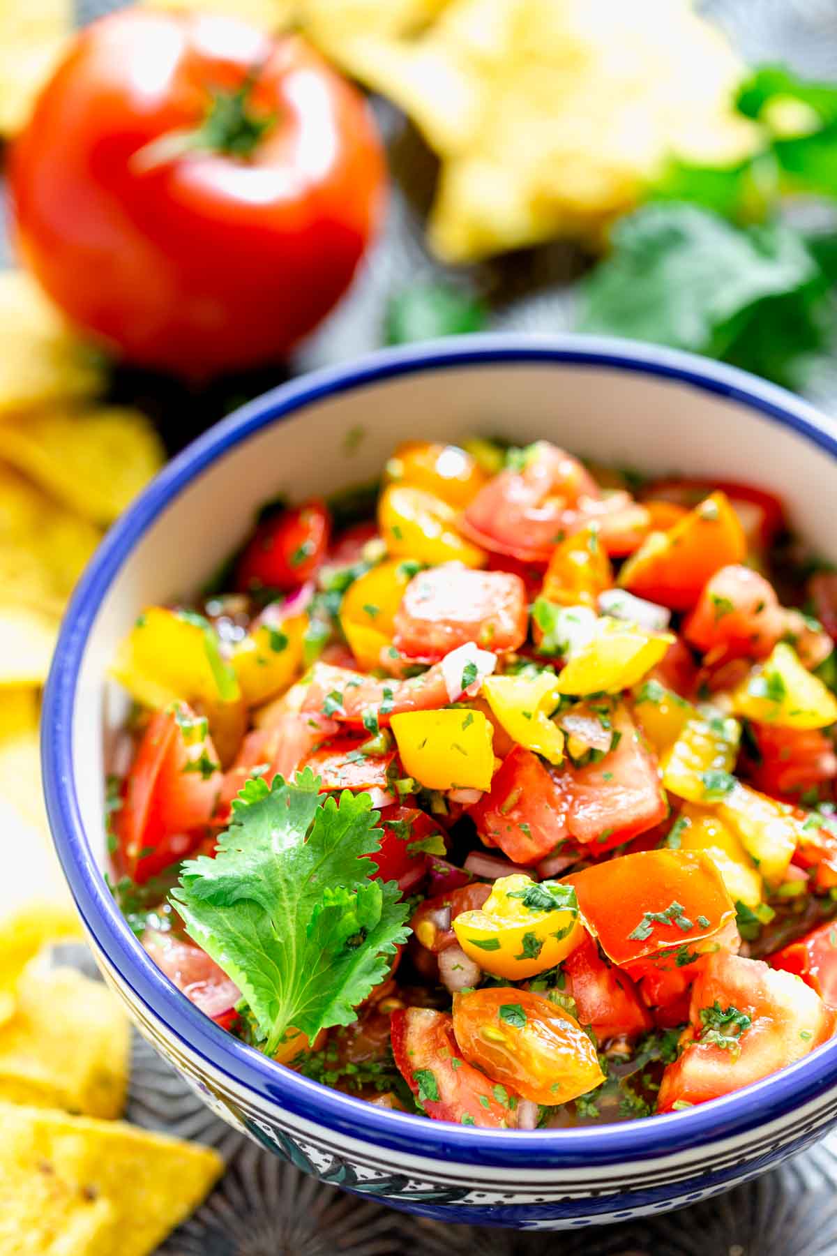 pico de gallo in a bowl with a tomato in the background