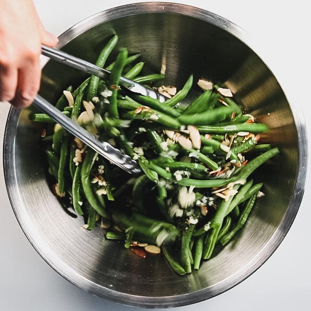 stirring the green beans in a bowl with tongs